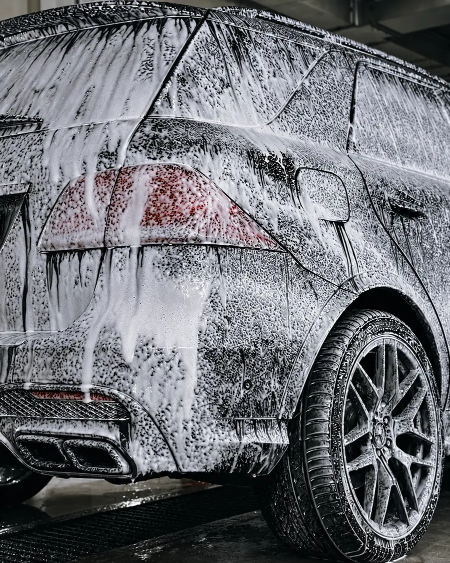 Dark SUV covered in thick snow foam during a pre-wash, close-up of rear taillight and wheel